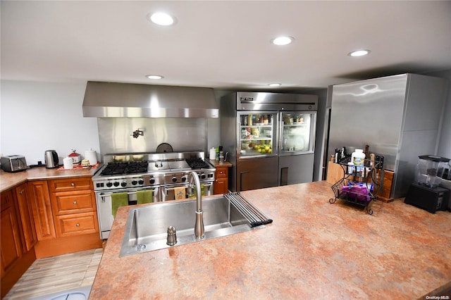 kitchen with sink, light wood-type flooring, wall chimney range hood, and high end appliances