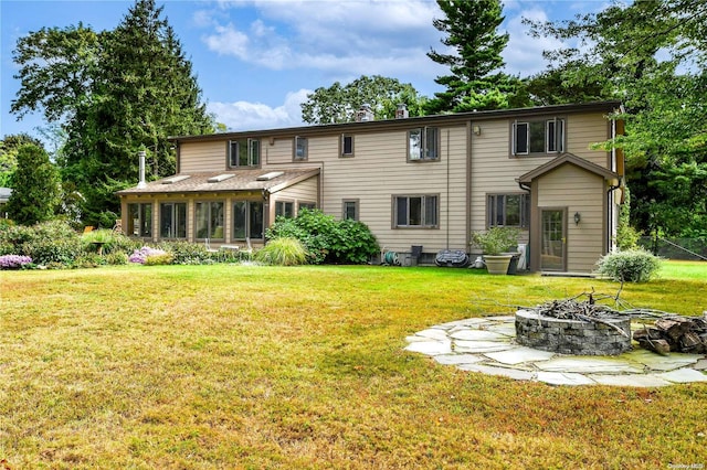 rear view of house with a yard, a fire pit, and a sunroom