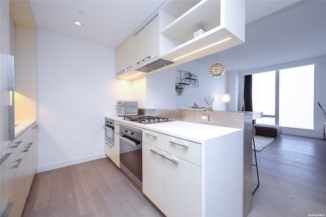 kitchen with decorative light fixtures, light wood-type flooring, white cabinetry, and appliances with stainless steel finishes