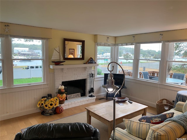 living room with wood-type flooring, a water view, a brick fireplace, and a healthy amount of sunlight