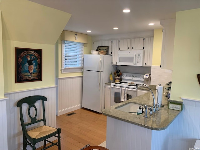 kitchen with white appliances, dark stone counters, white cabinets, sink, and light hardwood / wood-style floors