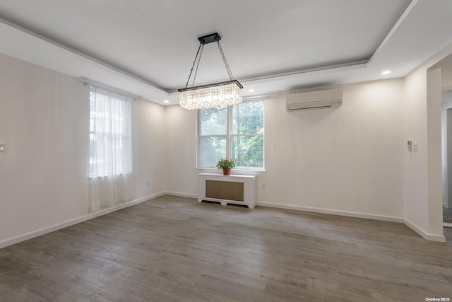 unfurnished dining area featuring a tray ceiling, a wall unit AC, wood-type flooring, a chandelier, and radiator heating unit