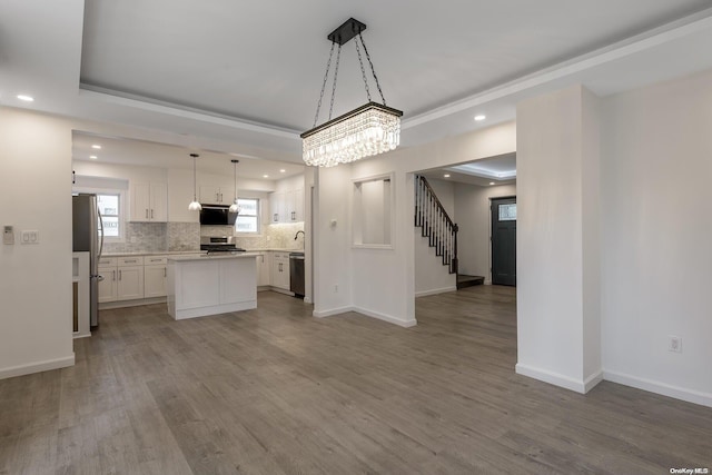 kitchen with white cabinetry, stainless steel appliances, range hood, pendant lighting, and wood-type flooring