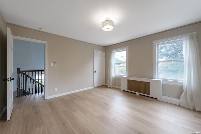 empty room featuring light wood-type flooring, radiator, and crown molding