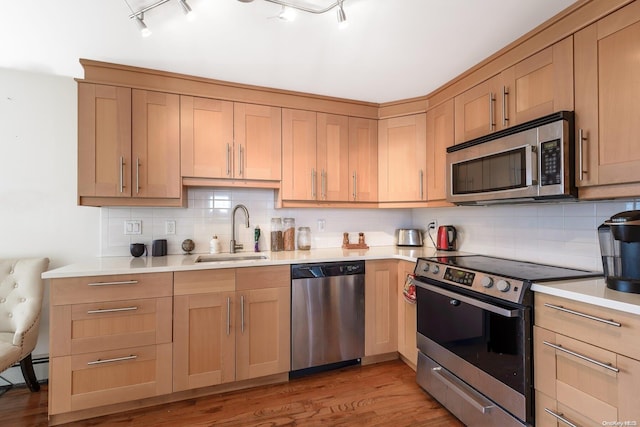 kitchen with sink, light hardwood / wood-style flooring, backsplash, track lighting, and appliances with stainless steel finishes