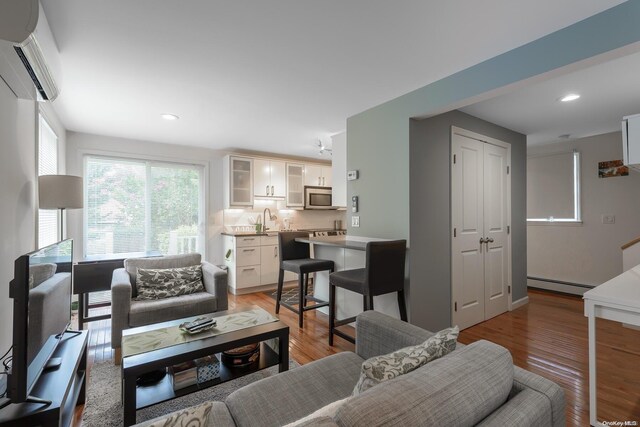 living room featuring light wood-type flooring, an AC wall unit, a baseboard heating unit, and sink