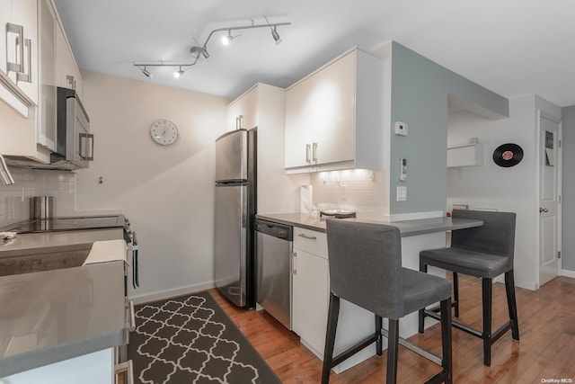 kitchen with white cabinets, backsplash, stainless steel appliances, and light hardwood / wood-style flooring