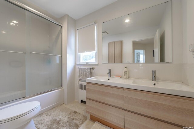 full bathroom featuring radiator heating unit, tile patterned flooring, combined bath / shower with glass door, backsplash, and toilet