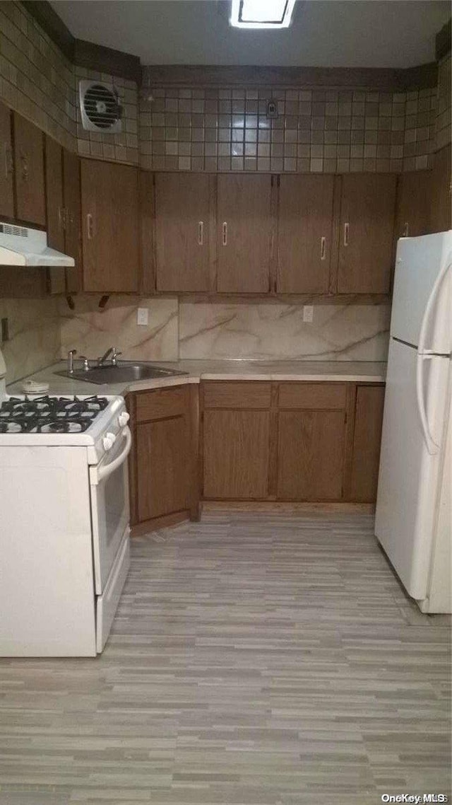 kitchen with light wood-type flooring, white appliances, tasteful backsplash, and sink