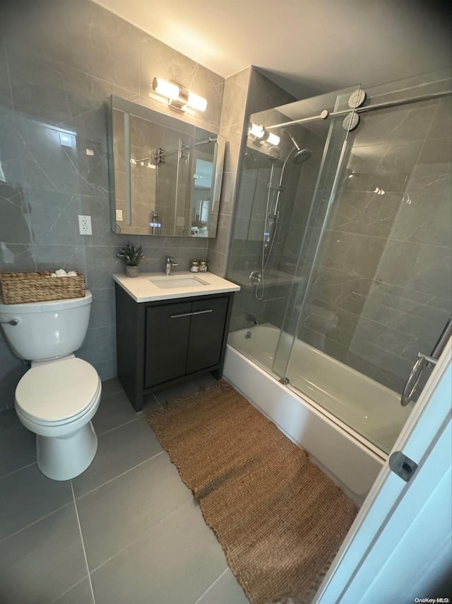 full bathroom featuring tile patterned floors, vanity, shower / bath combination with glass door, tile walls, and toilet