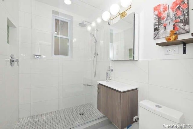 bathroom featuring a tile shower, tasteful backsplash, toilet, vanity, and tile walls