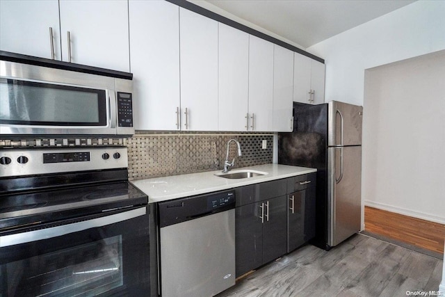 kitchen with backsplash, white cabinets, sink, appliances with stainless steel finishes, and light hardwood / wood-style floors