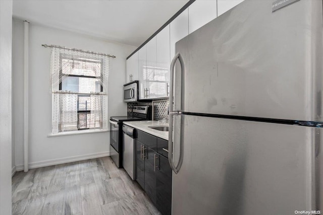 kitchen with backsplash, white cabinetry, stainless steel appliances, and light hardwood / wood-style flooring