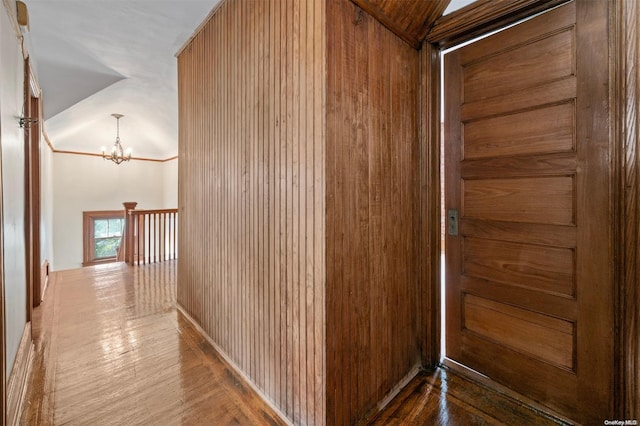 hallway featuring hardwood / wood-style flooring, vaulted ceiling, wooden walls, and a notable chandelier