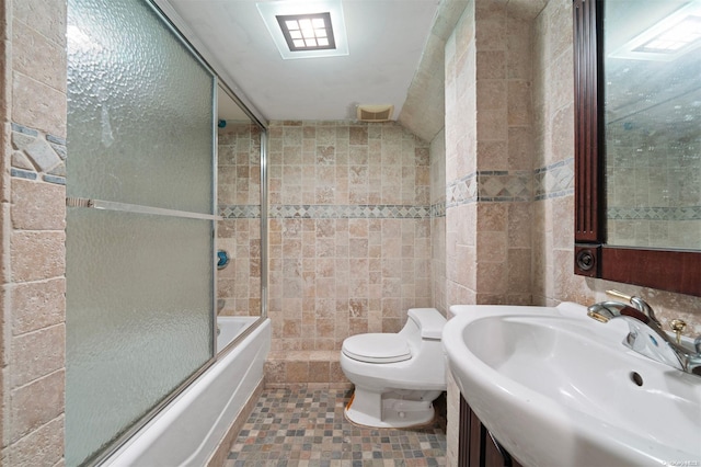 full bathroom featuring tile patterned floors, bath / shower combo with glass door, sink, tile walls, and toilet