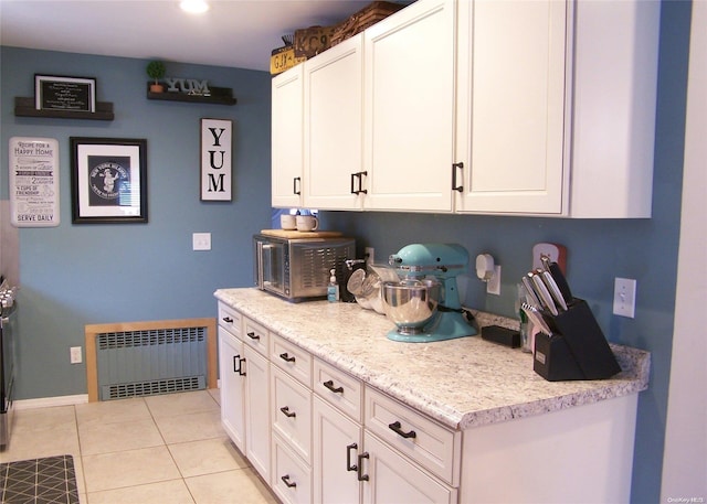 kitchen featuring white cabinets, light stone countertops, radiator heating unit, and light tile patterned floors