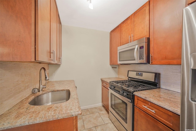 kitchen with tasteful backsplash, light stone counters, stainless steel appliances, sink, and light tile patterned flooring