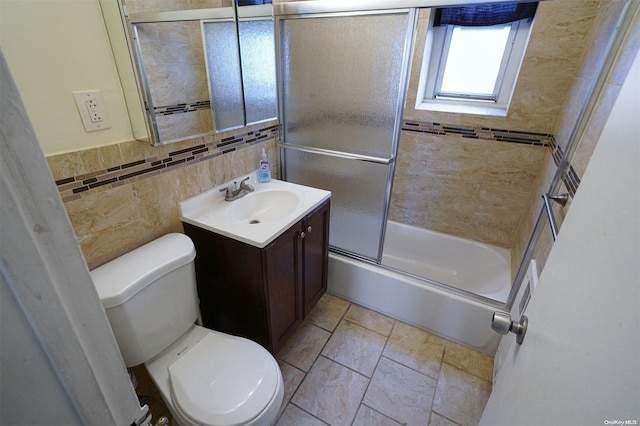 full bathroom featuring vanity, toilet, bath / shower combo with glass door, and tile walls