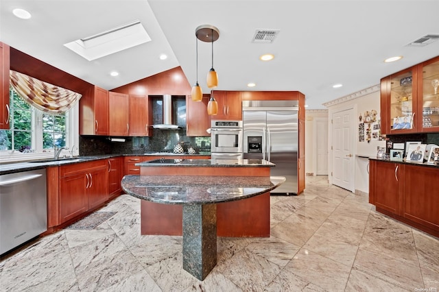 kitchen featuring wall chimney exhaust hood, hanging light fixtures, stainless steel appliances, dark stone countertops, and a kitchen island