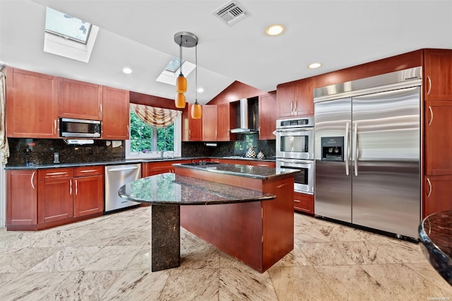 kitchen featuring a center island, wall chimney range hood, decorative light fixtures, vaulted ceiling with skylight, and appliances with stainless steel finishes