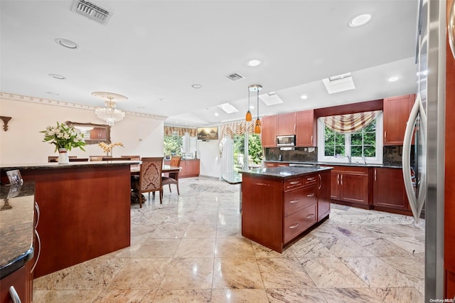 kitchen with appliances with stainless steel finishes, backsplash, decorative light fixtures, a notable chandelier, and a center island