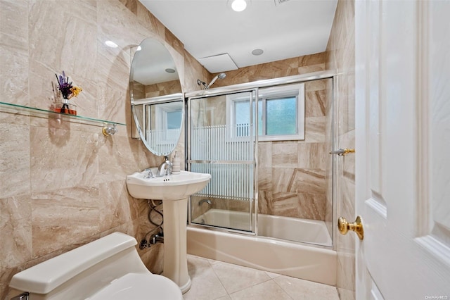 bathroom with tile patterned floors, combined bath / shower with glass door, tile walls, and toilet