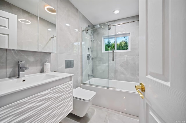 full bathroom with vanity, toilet, tile walls, and bath / shower combo with glass door