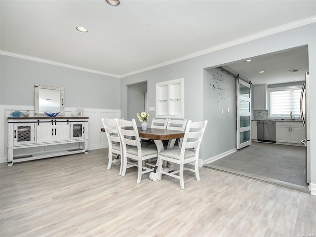 dining area featuring a barn door, crown molding, and light hardwood / wood-style flooring