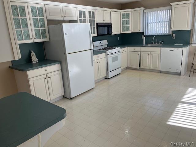 kitchen with dark countertops, white appliances, glass insert cabinets, and a sink