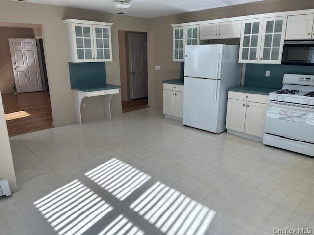 kitchen with white appliances, dark countertops, glass insert cabinets, and white cabinetry