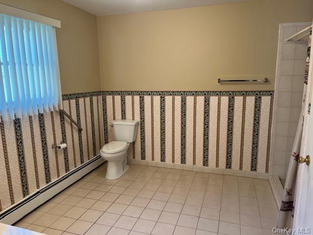 bathroom with wainscoting, toilet, baseboard heating, and tile patterned floors