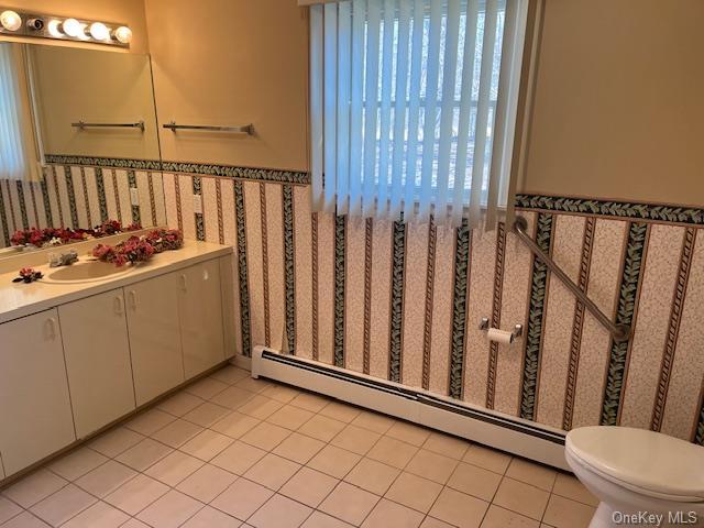 bathroom with a baseboard radiator, toilet, wainscoting, vanity, and tile patterned flooring