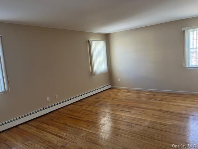 spare room featuring a baseboard radiator, baseboards, and wood finished floors