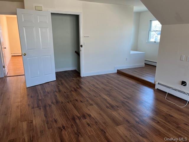 unfurnished bedroom with baseboards, a baseboard heating unit, and dark wood-type flooring