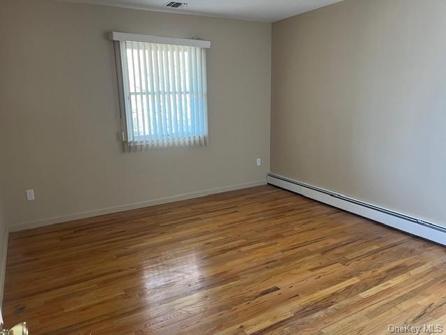 unfurnished room with a baseboard radiator, baseboards, and wood finished floors