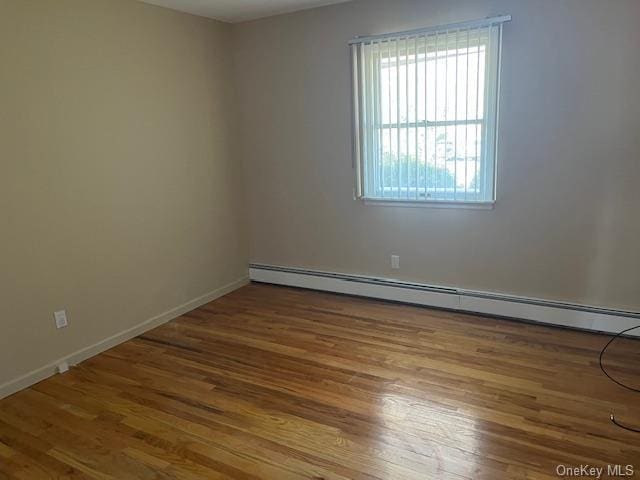 unfurnished room featuring baseboard heating, wood finished floors, and baseboards