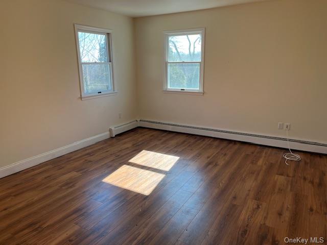 spare room featuring dark wood-type flooring, a healthy amount of sunlight, and baseboards