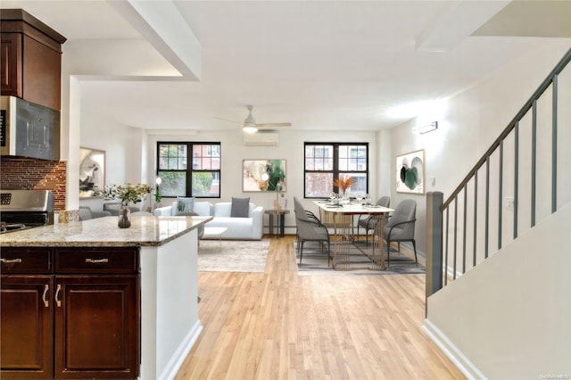 kitchen with light stone counters, stainless steel appliances, dark brown cabinets, a wall mounted air conditioner, and light wood-type flooring