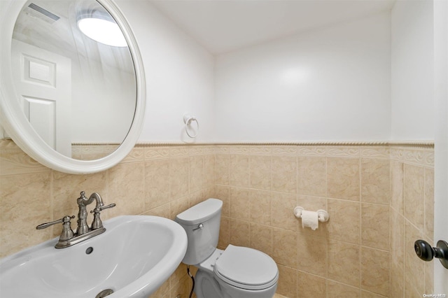 bathroom featuring wainscoting, toilet, tile walls, and a sink