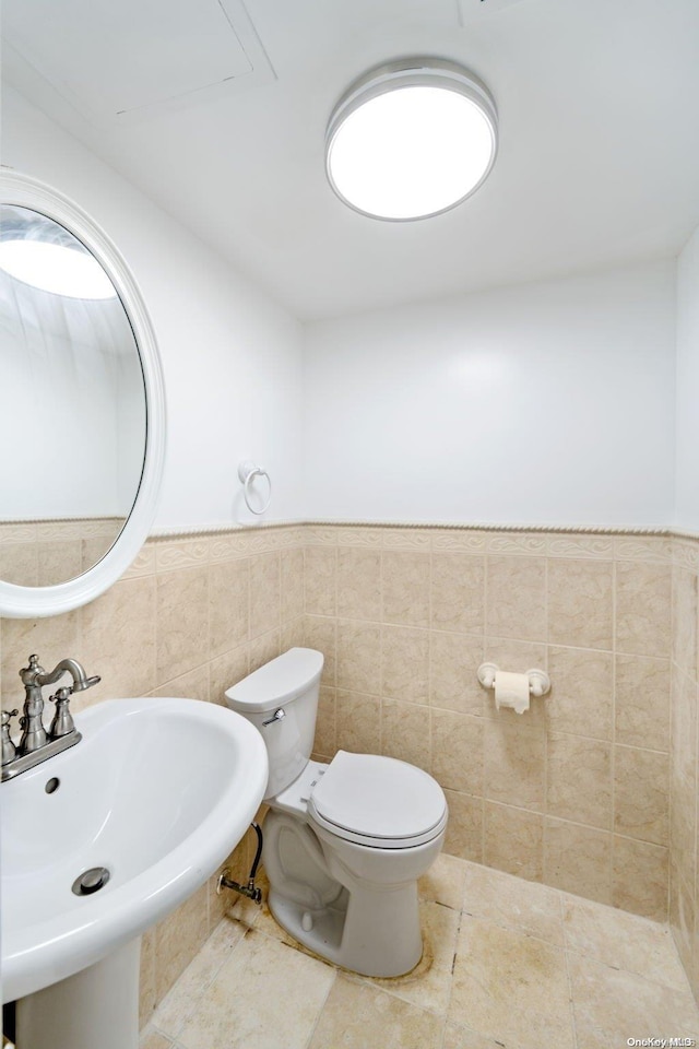 half bathroom featuring a sink, a wainscoted wall, toilet, and tile walls