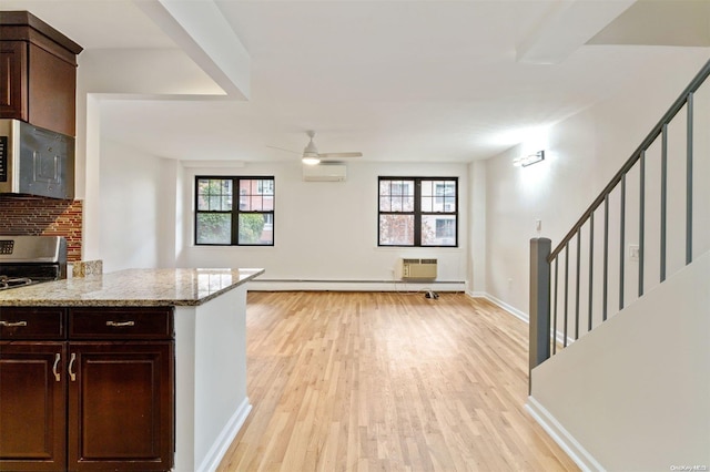 kitchen with light stone countertops, an AC wall unit, dark brown cabinetry, appliances with stainless steel finishes, and light wood-type flooring