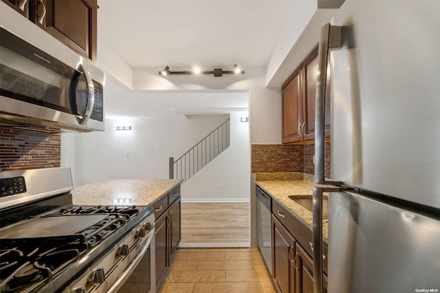 kitchen with light wood-type flooring, stainless steel appliances, baseboards, decorative backsplash, and light stone countertops