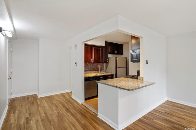 kitchen with light stone counters, freestanding refrigerator, a sink, light wood-style floors, and stainless steel dishwasher