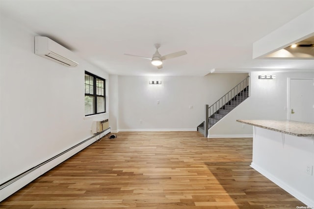 below grade area with light wood-type flooring, an AC wall unit, stairway, a baseboard radiator, and ceiling fan