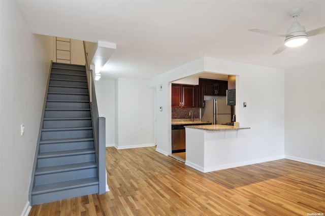 kitchen featuring light wood-type flooring, a peninsula, ceiling fan, appliances with stainless steel finishes, and tasteful backsplash