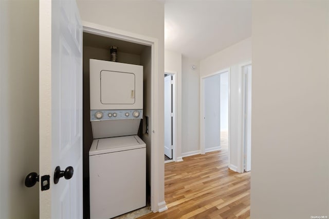 laundry room featuring baseboards, light wood-style floors, stacked washer and clothes dryer, and laundry area