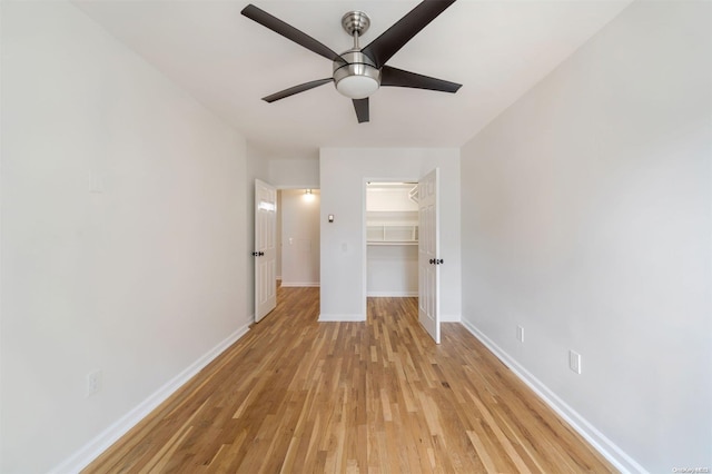 unfurnished bedroom with baseboards, light wood-style flooring, ceiling fan, a closet, and a walk in closet