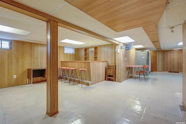 basement featuring bar, a paneled ceiling, and wood walls