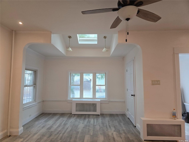 unfurnished living room with radiator, ceiling fan, a skylight, and light wood-type flooring