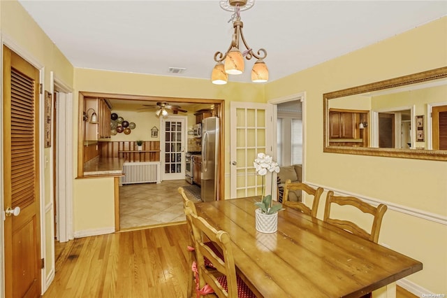 dining space featuring ceiling fan with notable chandelier, light wood-type flooring, and radiator